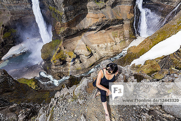 Eine junge asiatische Wanderin posiert für ein Porträt am Rande eines atemberaubenden Tals mit zwei Wasserfällen  bekannt als Haifoss  Island