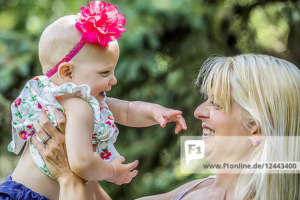 A beautiful young mother with long blonde hair enjoying quality time with her cute baby daughter in a city park on a summer day  Edmonton  Alberta  Canada