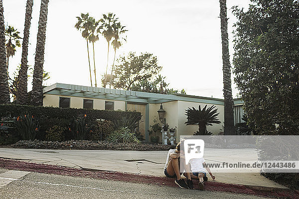 Zwei junge Mädchen sitzen auf einem Bordstein vor einem Haus; Los Angeles  Kalifornien  Vereinigte Staaten von Amerika