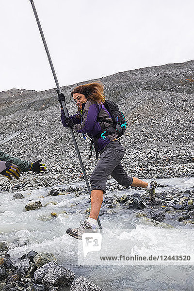 Eine Frau springt mit Hilfe einer Stange über einen reißenden Gletscherbach in der Nähe des Gulkana-Gletschers  Alaska  Vereinigte Staaten von Amerika