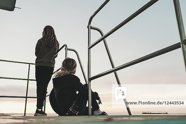 Zwei Mädchen sitzen in der Morgendämmerung auf einer Rettungsschwimmerstation und schauen auf den Ozean hinaus; Long Beach  Kalifornien  Vereinigte Staaten von Amerika