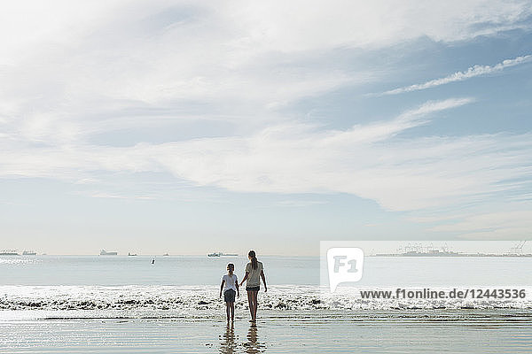 Zwei Schwestern  die an einem Strand zur Brandung hinausgehen; Long Beach  Kalifornien  Vereinigte Staaten von Amerika