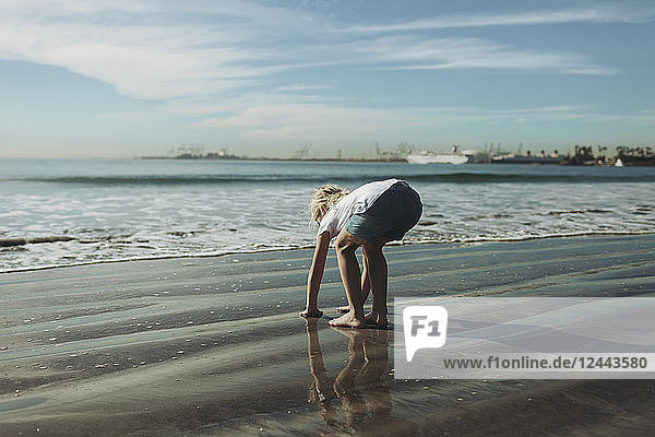 A young girl plays in the wet sand along the shoreline; Long Beach  California  United States of America