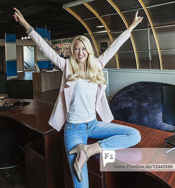 Schöne junge Geschäftsfrau mit langen blonden Haaren  die ihren Erfolg feiert und für die Kamera am Arbeitsplatz posiert  Edmonton  Alberta  Kanada