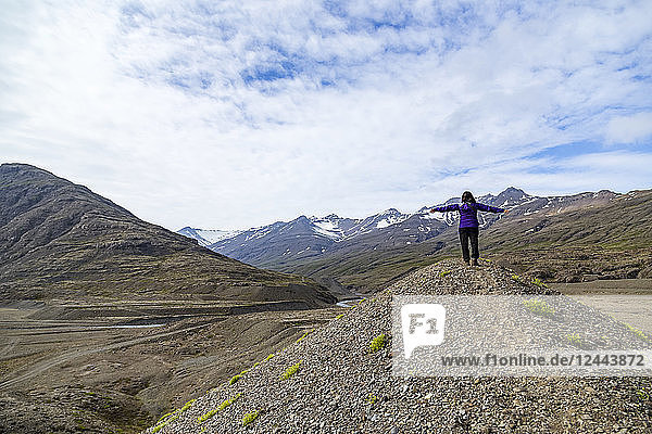 Eine Wanderin feiert die Natur mit ausgestreckten Armen auf dem Gipfel eines Hügels in der Berglandschaft Südislands  Island