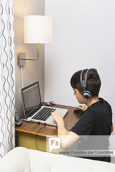 Ein kleiner Junge macht seine Hausaufgaben an einem kleinen Schreibtisch in seinem Haus und hört gleichzeitig Kopfhörer; Langley,  British Columbia,  Kanada