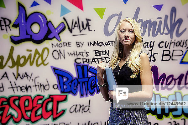 Junge Millennial-Geschäftsfrau mit ihrem Tablet vor einer bunten Wand mit motivierenden Graffiti  Sherwood Park  Alberta  Kanada