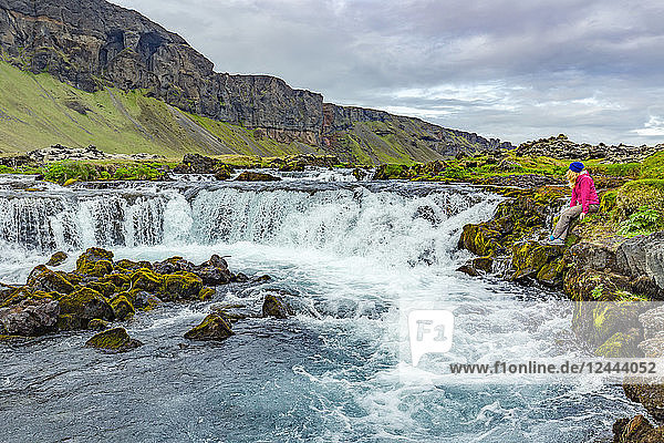 A female hiker poses for a photo on the edge of a waterfall,  Iceland