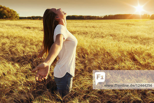 A woman stands in a wheat field with arms outstretched in surrender  Alberta  Canada