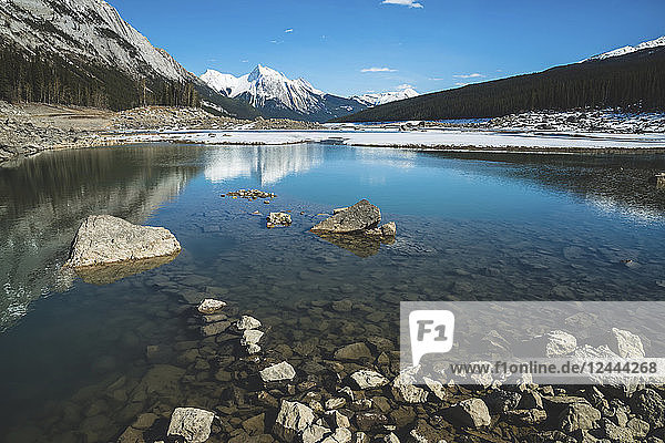 Snow on the lake and snow-capped rugged mountains peaks reflected in the water  Jasper National Park; Alberta  Canada