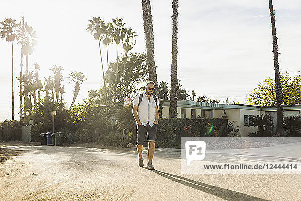 Mann geht mit einem Rucksack auf einer Wohnstraße in einem tropischen Klima; Long Beach  Kalifornien  Vereinigte Staaten von Amerika