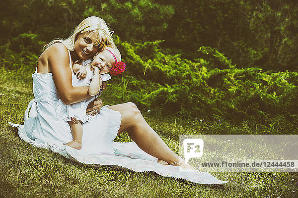 Eine hübsche junge Mutter mit langen blonden Haaren genießt die Zeit mit ihrer süßen kleinen Tochter auf einer Decke im Gras eines Stadtparks an einem Sommertag  Edmonton  Alberta  Kanada