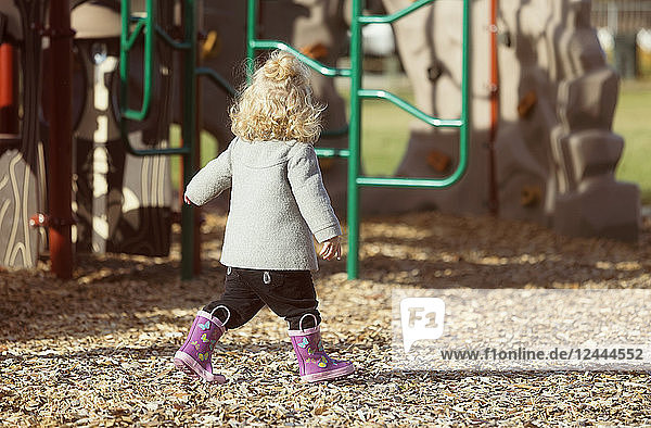 Ein süßes junges Mädchen  das im Herbst in Gummistiefeln über einen Spielplatz läuft  Spruce Grove  Alberta  Kanada