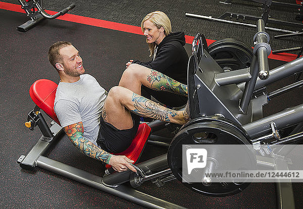 A personal trainer coaching a young man doing leg presses at a fitness facility  Spruce Grove  Alberta  Canada