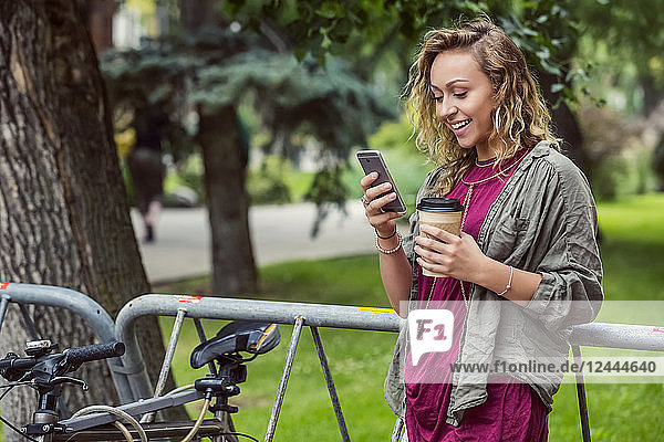 Porträt einer hübschen jungen Studentin  die sich auf einem Fahrradständer auf dem Campus anlehnt und Texte auf ihrem Smartphone liest  Edmonton  Alberta  Kanada