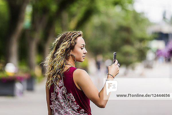 Eine schöne junge Frau  die eine Straße in der Nähe eines Universitätscampus entlangläuft und mit ihrem Smartphone Videoaufnahmen macht  Edmonton  Alberta  Kanada