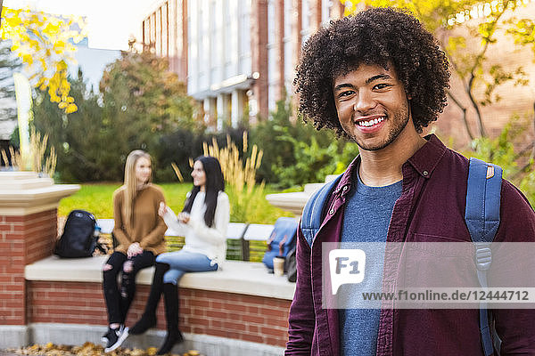 Porträt eines jungen afroamerikanischen Universitätsstudenten  der mit seinen Freunden im Hintergrund auf dem Universitätscampus posiert  Edmonton  Alberta  Kanada