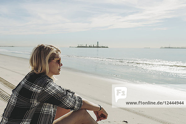 A woman sits on a beach looking out to the water; Long Beach  California  United States of America