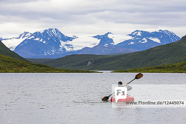 A man paddles a packraft across Landmark Gap Lake with the Alaska Range in the distance  Alaska  United States of America