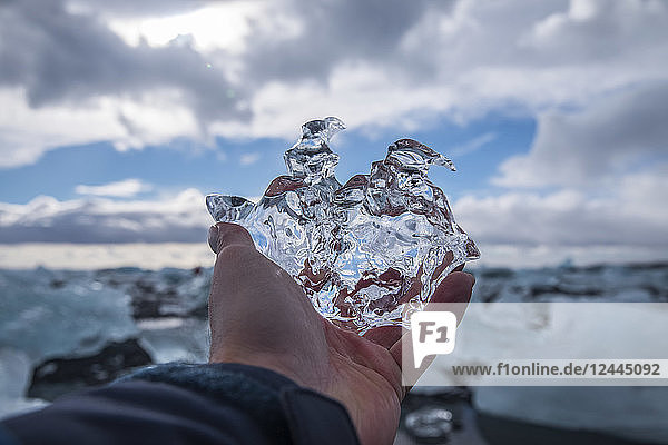Mann hält ein Stück Eis in Jokulsarlon  Südküste  Island