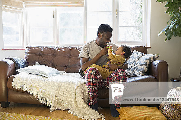Affectionate father in pajamas cuddling with baby son on living room sofa