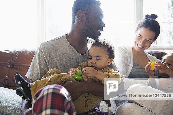Glückliche multiethnische Familie im Schlafanzug kuschelnd auf dem Sofa