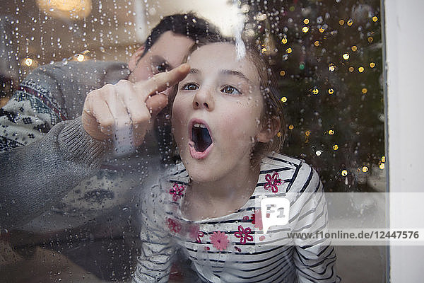Verspielter Vater und Tochter malen im Kondenswasser an einem nassen Winterfenster