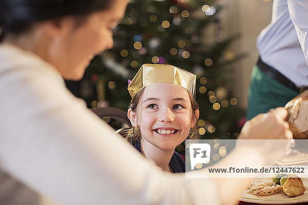 Lächelndes Mädchen mit Papierkrone genießt das Weihnachtsessen