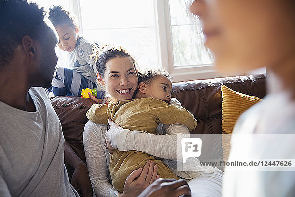 Happy mother cuddling baby son  relaxing with family on living room sofa