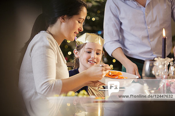 Mother serving carrots to daughter in paper crown at Christmas dinner