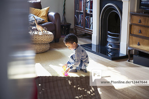 Junge im Schlafanzug spielt mit Spielzeug auf dem Boden im Wohnzimmer