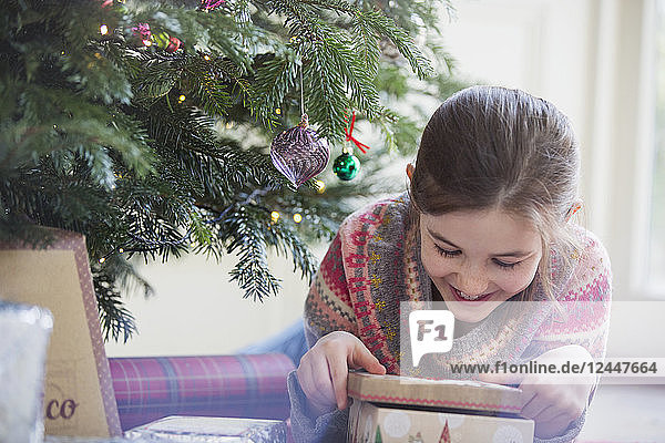 Lächelndes  neugieriges Mädchen öffnet Weihnachtsgeschenk