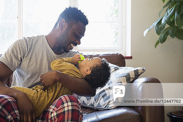 Affectionate father cuddling with baby son on living room sofa