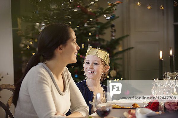 Glückliche Mutter und Tochter in Papierkrone bei Kerzenschein Weihnachtsessen Tisch