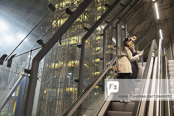 Business people with suitcase talking on urban escalator at night