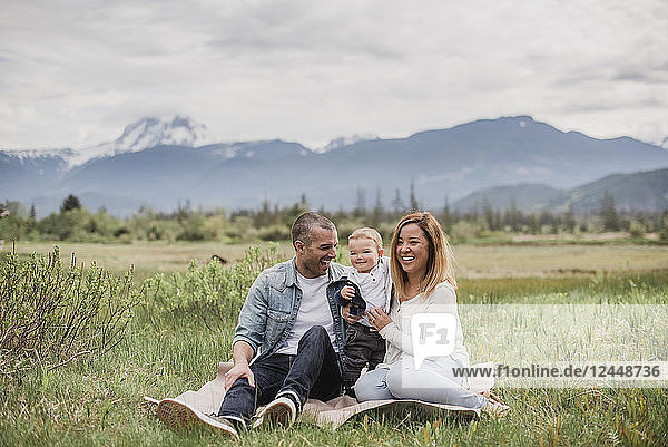Parents and baby son sitting in rural field with mountains in background