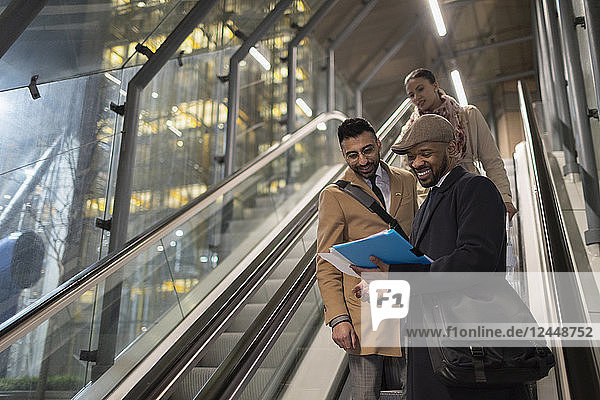 Businessmen discussing paperwork on urban escalator at night
