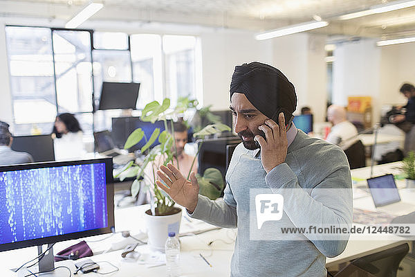 Indian computer programmer in turban talking on smart phone in office