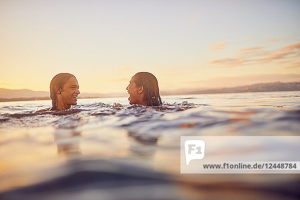 Young couple swimming in ocean at sunset