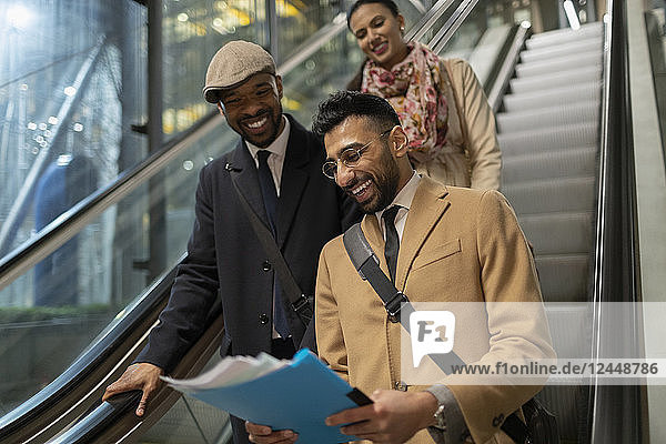 Smiling business people reading paperwork on escalator