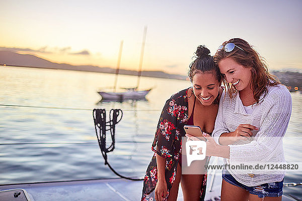 Young women friends using smart phone on boat