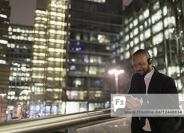 Businessman with headphones using digital tablet on urban pedestrian bridge at night