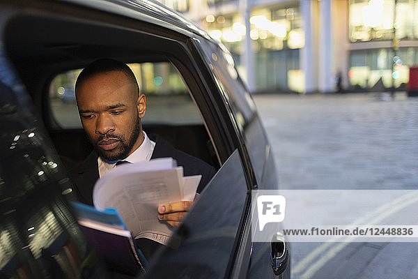 Businessman reading paperwork in crowdsourced taxi at night