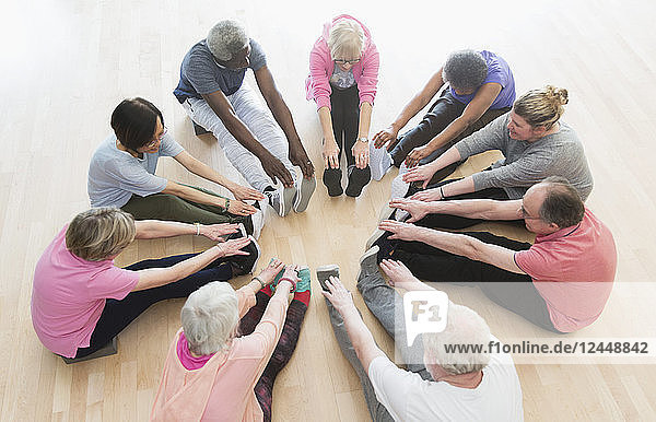 Active seniors stretching legs in circle in exercise class