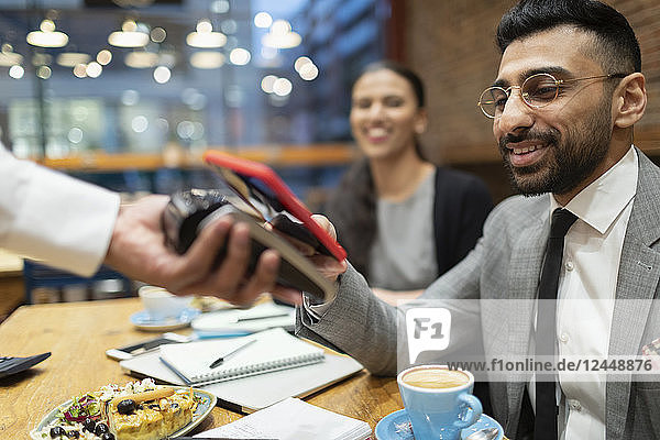 Businessman paying with smart phone contactless payment in cafe