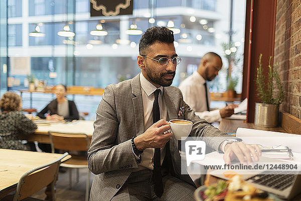 Focused businessman drinking coffee and working at laptop in cafe