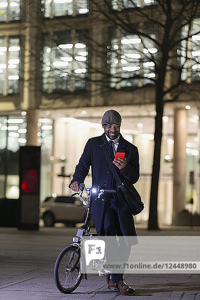 Businessman with bicycle using smart phone on urban sidewalk at night