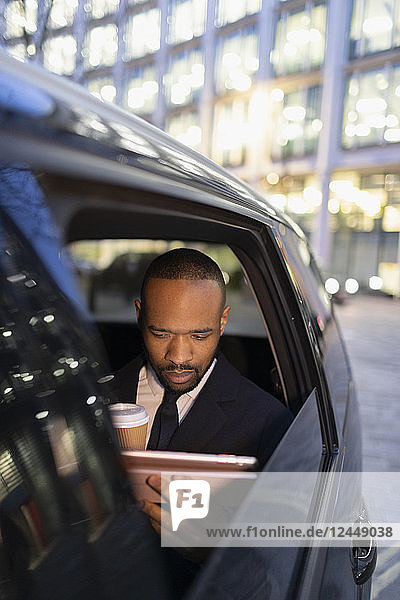 Businessman drinking coffee  using digital tablet in crowdsourced taxi