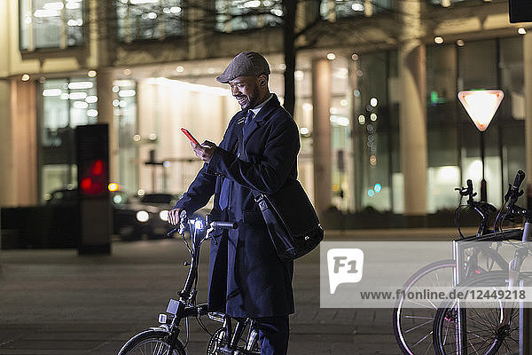 Businessman with smart phone and bicycle on urban street at night