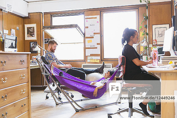 Creative designers relaxing in hammock in office